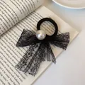 Elegant black lace bow hair tie with pearl center placed on an open book - Lace Pearl Bow Style