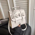 Chic beige leather backpack with bow knots and pearl charm shown in hand - With Pendant / White