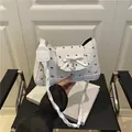White underarm bag featuring delicate black bow prints and a silver heart charm - White