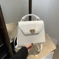 White faux leather square handbag with golden twist lock and top handle shown in hand - White