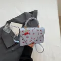 Lichtblauwe crossbodytas met kersenprint en een uniek gedraaid handvat bovenaan - Blauw