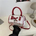 Sweet red and white barrel bag with bow detail and heart pendant in a lifestyle setting - Red