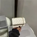 Mini cream quilted crossbody bag with gold chain strap held in a hand stylishly - White