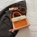 Orange and cream leather handbag with gold metal clasp on a grey blazer background - Orange