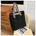 Detalle del bolso tote de lona negra con correas de rayas y logotipo de pétalo plateado - Negro
