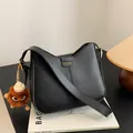 Minimalist black arched shoulder bag with gold logo and plush monster charm detail - With Pendant / Black