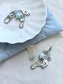 Detail of blue beaded phone charms with silver lobster clasp and minimalist fish motif - Buckle Style / Abundance Theme