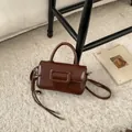 Detail view of chocolate brown crossbody bag with large square buckle and woven strap - Brown with Pendant