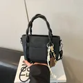 Chic black crossbody bag with woven handles, front pocket and chocolate charm accessory - Black