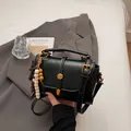 Vintage black Boston handbag with gold buckle and wooden bead charm on a grey blazer - Black