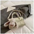 Chic beige crossbody square bag with plush bunny charm on grey blazer and book - Rice Grey With Pendant