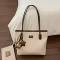 Detail of a cream faux leather tote bag with chocolate brown handles and a teddy bear charm - Cream White With Pendant