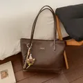 Macro shot of brown PU leather tote bag texture with brand label and bear charm - Coffee With Pendant