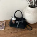 Minimalistische schwarze Tragetasche mit Anhänger und Schultergurt auf Holztisch - Mit Anhänger / Schwarz