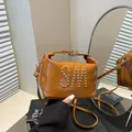 Borsa a tracolla quadrata marrone in pelle con logo SM borchiato in un ambiente minimalista - Marrone