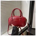 Close-up of a red glossy patent leather Boston bag with gold fashion lettering and handles - Red