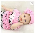 Reborn baby doll in pink cow print outfit with floral headband on white plush mat - Pink / 55 cm