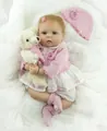 Lifelike reborn baby doll in pink knit cardigan and skirt with small plush bear accessory - Pink
