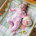 Close-up of smiling reborn baby doll in pink romper inside a wooden crib - Pink