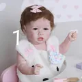 22 inch lifelike reborn baby Saskia doll with brown curly hair and pink bow headband - Pink Bear Plush Vest Style / Blue Eyes