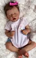 Nahaufnahme einer schlafenden 18-Zoll Reborn-Puppe in rosa Streifen auf Kunstfell - Stoffkörper