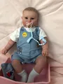 Detailed close-up of 60cm reborn baby boy doll in striped overalls sitting in a pink basket - As Shown / 60 cm