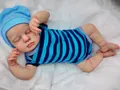 Detail of reborn baby doll in sleeping pose with striped romper and blue cotton hat - Full Silicone Boy