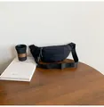 Detail of a black nylon crescent waist bag on a wooden table with a minimalist setup - Black