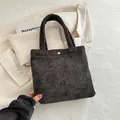 Minimalist dark grey woven tote bag with metallic gold buckle on a stylish beige blazer - Black