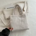 Minimalist beige woven tote bag with gold snap button on chic textured blazer background - White