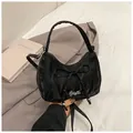 Close-up of black wrinkled texture handbag with large decorative bow and silver logo - Black