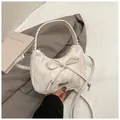 Detail of white textured dumpling bag with bow knot and metal logo on a soft bed - White