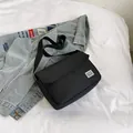 Minimalist black canvas messenger bag with Black Rice logo on a casual blue jacket - Black