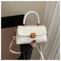 Elegante bolso de mano blanco con hebilla dorada y asa superior en un ambiente sobrio - Blanco
