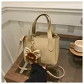 Detail of khaki lychee textured bucket bag with fluffy bow charm on a wooden table - Khaki