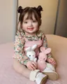 Detailansicht der Reborn-Babypuppe in rosa Latzhose mit Plüschhasen-Spielzeug - Großer Stoffkörper / Rosa Blumig