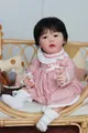 Lifelike 23-inch reborn baby doll in pink polka dot dress sitting in a wicker cradle - 23 Inches / Cloth Body