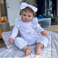 Lifelike 60cm Maddie reborn baby doll with brown hair and white bow headband in a seated pose - Realistic Baby with White Romper / 60cm Cloth Body
