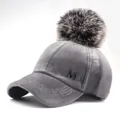 Detail of grey plush baseball cap with faux fur pompom and metal M logo accent - Adjustable / Gray (6-Panel Gray Pom-pom Snap Style) / Adult