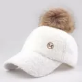 Close-up of fluffy white lamb wool baseball cap with brown faux fur pom pom and golden M logo - Adjustable / White With Natural Pom Pom