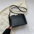 Minimalist black matte crossbody bucket bag with golden buckle on a white blazer background - Black