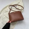 Elegant brown leather crossbody bag with gold metal accents on a beige blazer backdrop - Brown