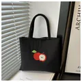 Detail of red apple embroidery on a black nylon tote bag with fine fabric texture - Black