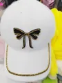 Close-up of plush white baseball cap featuring black bow and golden bead chain detail - Bow Style / White