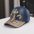 Detailed close-up of a blue denim baseball cap featuring an ornate rhinestone fleur-de-lis - Adjustable / Dark Blue