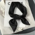 Detail of a black satin neck scarf tied in a bow showing smooth silk-like texture - One Size / Black
