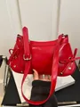 Detalle del bolso de hombro en charol rojo con lazos decorativos y hebilla de metal plateado - Rojo