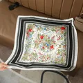 Elegante foulard in seta bianca a fiori con bordo nero posato su un divano in pelle - Floreale Francese Bordo Nero