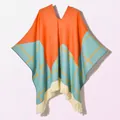 Detail of color-block knit poncho with orange and blue patterns and cream tassel trim - Pullover Five Star Plaid Orange