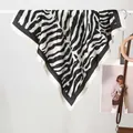 Dettaglio di un foulard in raso con motivo zebrato appeso a un supporto in stile moderno - Zebra Nero e Bianco / 70x70cm